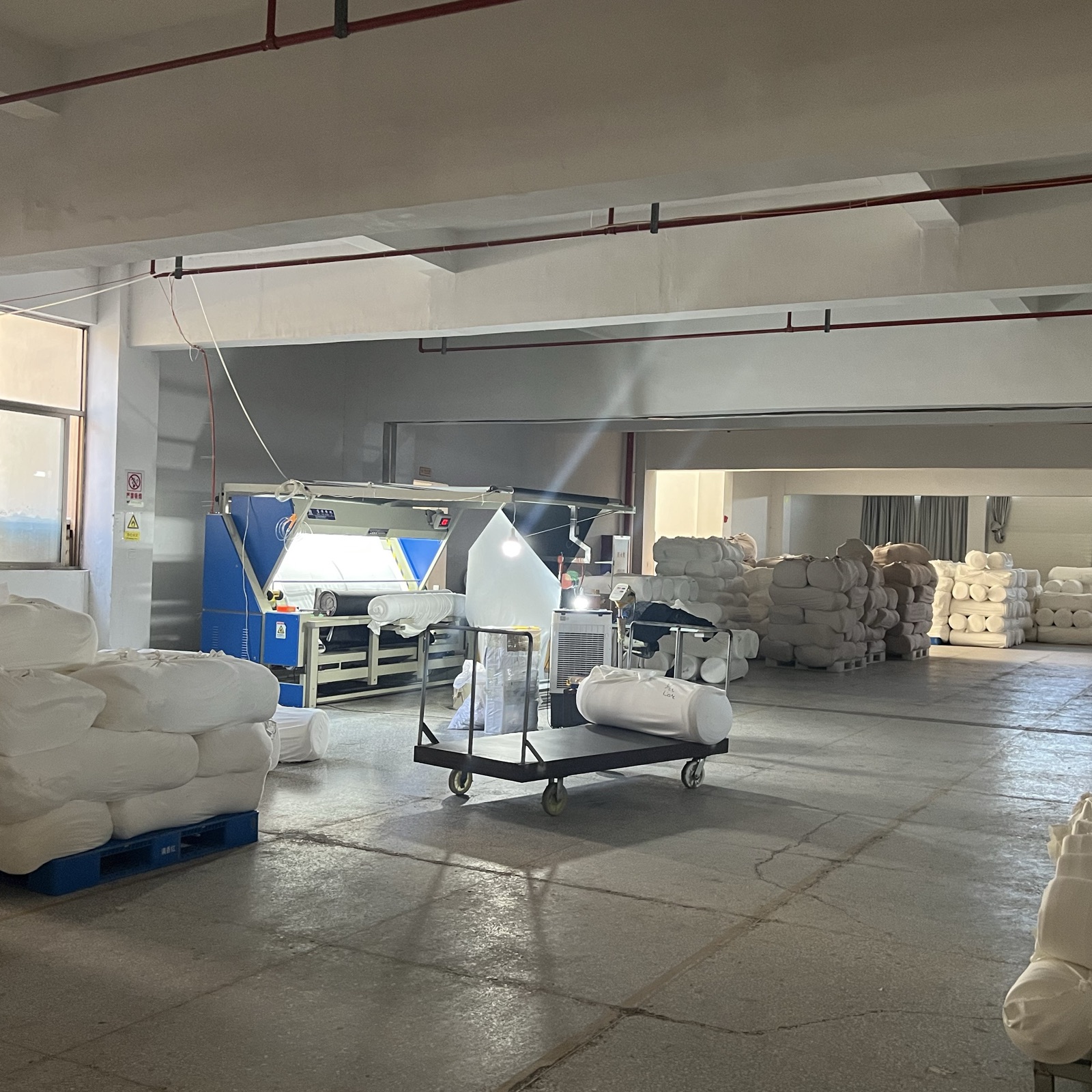 White knitted fabric rolls beside fabric inspection equipment